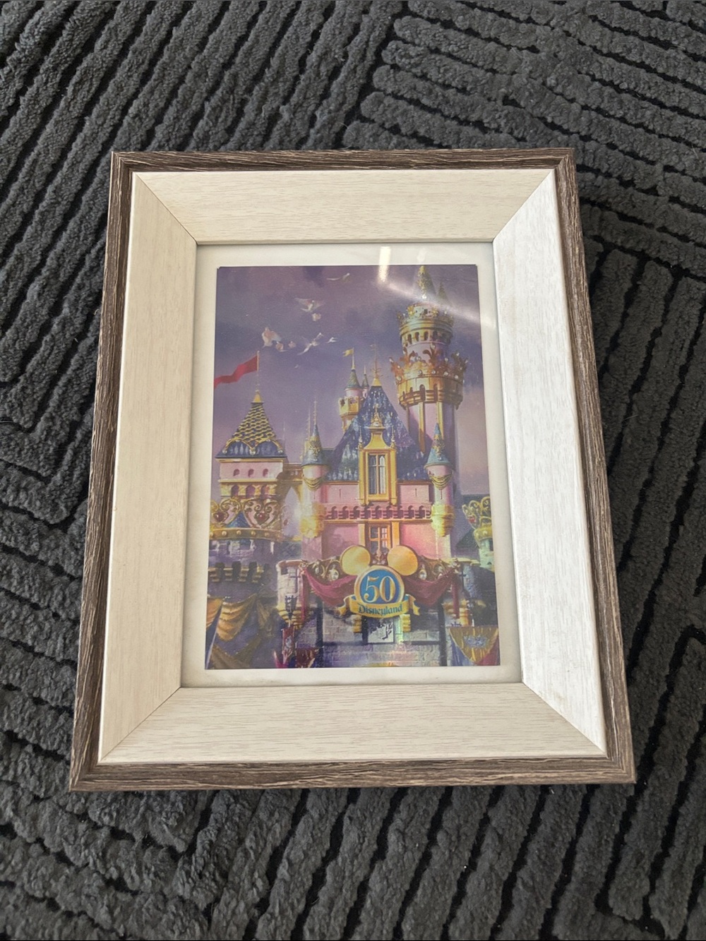 Disneyland 50th anniversary postcard in a frame.
